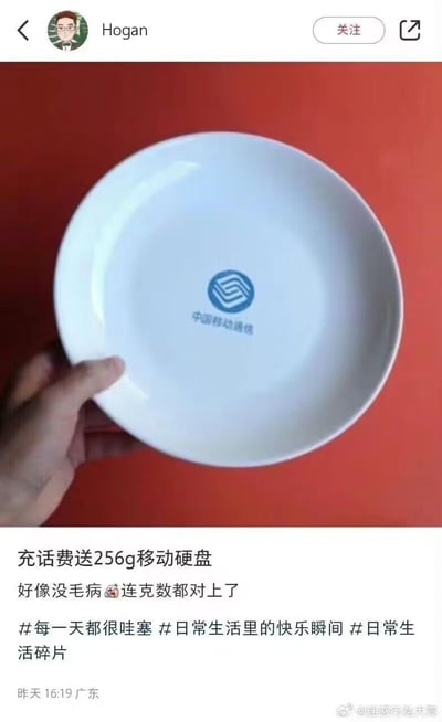 这是一张微博用户发布的搞笑梗图，图中展示了一只手拿着印有中国移动通信标志的白色盘子，配文称“充话费送256g移动硬盘”，玩了谐音梗：将存储设备“移动硬盘”谐音成“移动的硬盘子”（餐具），256G在这里指代盘子的重量克数，而非存储容量，通过这种反差感制造出搞笑效果，调侃运营商的充话费送礼品活动。