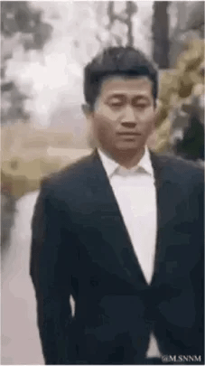 这是一段动态GIF图，内容是演员吴京身着黑色西装搭配白色衬衫，在户外林间小路上行走，面部表情严肃平淡。该动图常被用作网络表情包，多用于聊天场景中表达无语、无奈的情绪，或是单纯作为场景过渡素材，图中没有双关、谐音梗或暗示类内容。
