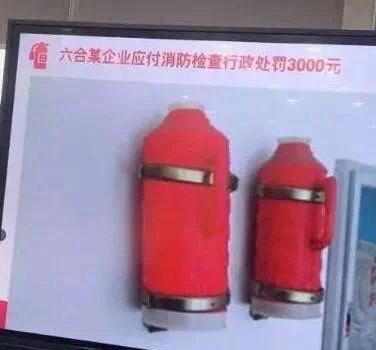 这是一张经过P图改编的屏幕截图，上方配有文字“六合某企业应付消防检查行政处罚3000元”，下方展示了两个被改装成灭火器外观的红色暖水瓶，通过给暖水瓶套上红色外壳、加装金属箍来伪装成灭火器，以此调侃该企业用如此荒唐的方式敷衍消防检查，最终被处以行政处罚的讽刺又搞笑的场景，凸显了这类企业对安全检查的漠视行为。