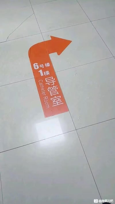 这是一张医院地面的实拍照片，地面上贴有橙色箭头形状的导视标识，箭头指向右侧，标识上标注了“6号楼 1楼 导管室 Catheter Room”，用于指引前往导管室的方向，没有双关、谐音梗或暗示内容。