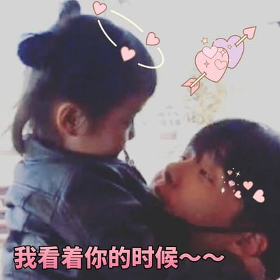 图片中展示了韩国童星权律二与另一个小朋友的温馨拥抱场景。权律二扎着小发髻，穿着深色外套，正温柔地抱着另一个孩子。图片添加了可爱的粉色爱心、丘比特之箭和闪光等装饰元素，底部配有文字'我看着你的时候～～～'，营造出温暖治愈的氛围。