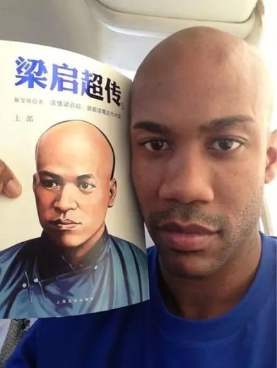 图中右侧是前NBA球星、CBA传奇外援斯蒂芬·马布里，他手持一本《梁启超传》，将书籍封面与自己的脸部并排摆放。二者均为光头造型，面部轮廓、眉眼形态甚至神态都高度契合，形成了跨越时空的趣味撞脸效果，画面充满巧合带来的幽默感，让人忍俊不禁。