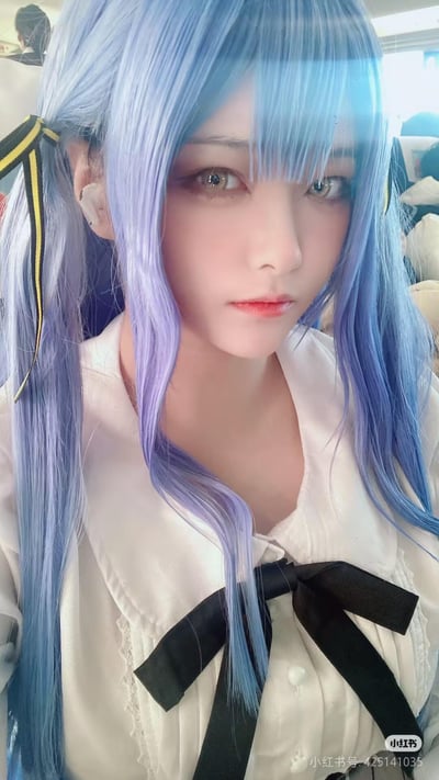 这是一张竖屏拍摄的cosplay自拍照片，图中人物佩戴蓝紫渐变的双马尾假发，用黄黑条纹发带将两侧头发束起，身着带有黑色蝴蝶结的白色学院风衬衫，耳朵上戴着白色蓝牙耳机，眼神清冷平静地看向镜头。背景环境看起来像是在公共交通工具的车厢内，整体造型精致，还原了二次元角色的风格气质。