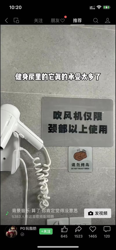 这是一张抖音视频的截图，画面展示了健身房浴室的挂墙式白色吹风机，旁边配有两块提示牌：一块较大的金属色提示牌写着“吹风机仅限颈部以上使用”，下方还有一块带卡通烤鸡图案的小提示牌，配文“请勿烤鸟”。画面上方有白色加注文字“健身房里的它真的承受太多了”，调侃健身房中存在用吹风机吹颈部以下身体部位，甚至用低俗玩笑暗指的不文明使用行为，用夸张的提示牌来吐槽这类离谱操作，十分搞笑。
其中“请勿烤鸟”是谐音梗，“烤鸟”暗指用吹风机吹隐私部位，是用玩笑式的低俗暗示来规范使用行为。
