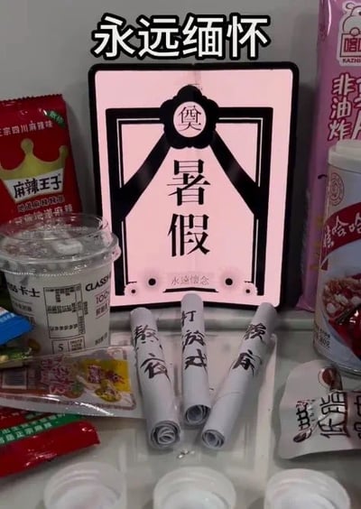 图片展示了一场为暑假结束举办的趣味“祭奠仪式”。画面中央是一块粉色背景的黑色边框牌位，上书“奠 暑假”，顶部有“永远缅怀”四个大字。牌位周围摆放着多种零食，包括麻辣王子辣条、卡士酸奶杯、嗨吃家酸辣粉桶、非油炸薯片等，前方还整齐摆放着三卷写有“熬夜”“打游戏”“赖床”字样的白色纸条，模拟祭奠时的纸钱。整体通过夸张的“追悼”形式，幽默表达了学生群体对暑假结束的不舍与无奈情绪。
