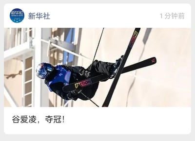 这是一张新华社在社交媒体发布的新闻图片，展示了滑雪运动员谷爱凌在比赛中完成空中翻转动作的瞬间。图片中，谷爱凌身着蓝色比赛服和头盔，双脚踩滑雪板在空中呈倒立姿态，背景可见赛场设施。图片下方配有文字“谷爱凌，夺冠！”，传达其夺冠的喜讯。