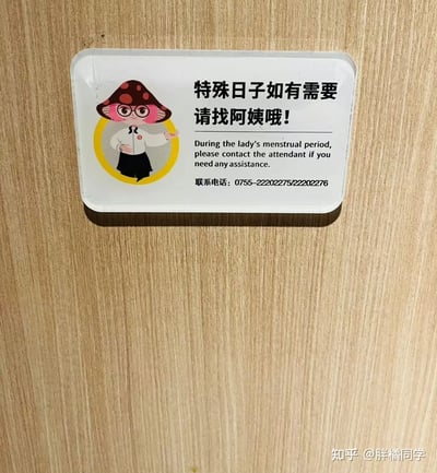 这是一张贴在墙上的温馨提示牌，针对女性特殊生理期（经期）提供求助引导。牌子上有卡通阿姨形象，采用中英文双语，且有联系电话，内容温和贴心，适合公共卫生间等场景，体现对女性的关怀与便利。没有出现谐音梗、双关或暗示等元素。