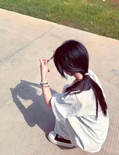 一位扎着低马尾的女生蹲在户外带有纹路的水泥步道上，身着宽松的白色短袖套装与白黑拼色板鞋，双手比出特定手势，在阳光的照射下，地面投射出一只猫咪形状的手影。整体画面氛围轻松治愈，充满生活小趣味。
无谐音梗、双关或暗示内容。