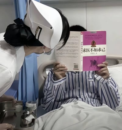 医院病房场景中，一位身着白色护士服、头戴护士帽的护士正俯身靠近病床上的患者。患者穿着蓝白条纹病号服，双手捧着一本封面为粉色的书籍《求医不如求己》，书本几乎完全遮挡了面部。图片通过场景与书本标题的反差制造幽默效果：患者在医院接受治疗时，却阅读着主张'求医不如求己'的书籍，形成强烈的讽刺意味，暗示了对过度依赖自我诊疗观念的调侃。