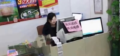 这是一张拍摄于体育彩票店内的照片，柜台后的工作人员坐在电脑设备前，面带笑意看向镜头方向。设备上贴着一张粉色手写纸条，写着“国足送钱 机会难得”；背景墙上的体育彩票宣传海报标注着“3亿大派奖！头奖最高1000万”。
这张图通过玩梗调侃国足的比赛表现，反向暗示购买国足输的彩票容易中奖，仿佛是“送钱”的机会，戳中球迷的笑点。