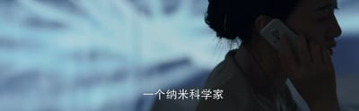 这是一张影视截图，画面右侧呈现一位头发盘起的女性，她正将手机贴在耳边进行通话，神情专注，背景是模糊的冷色调光影，营造出沉静的氛围。画面下方配有字幕“一个纳米科学家”，表明通话内容中提及了该身份的人物。