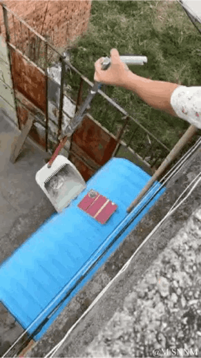 这是一个视觉错位的动态GIF图，画面中一只手握着锅铲，从拍摄视角看，锅铲的位置刚好对着下方蓝色板子上的物品，营造出要铲走这些物品的错觉，但实际上锅铲和物品不在同一平面，是利用视角差制造的趣味视觉效果，让人产生误解。