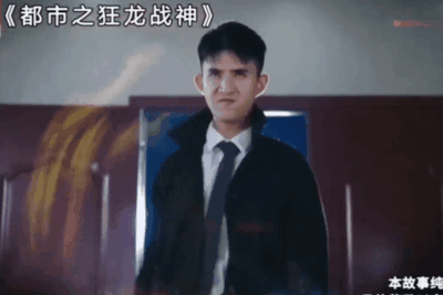 图片为网络热梗“龙王赘婿”系列广告的经典截图，出自《都市之狂龙战神》。画面中演员管云鹏身着黑色外套、白色衬衫和领带，表情严肃地站立，背景有黄色火焰特效，上方有标题文字“《都市之狂龙战神》”，底部标注“本故事纯属虚构”。该场景体现了“卑微赘婿即将揭露身份、逆袭打脸”的爽文套路，是2020年爆红的“歪嘴战神”文化的代表性画面之一。