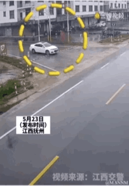 这是一段动态画面，展示了江西抚州一处道路旁的场景：一辆白色小轿车不慎驶入由多个黄色路障围成的圆圈内，被困其中，画面带有文字标注，说明发布时间为5月23日，来源为江西交警，整体呈现出一种让人哭笑不得的趣味交通场景。