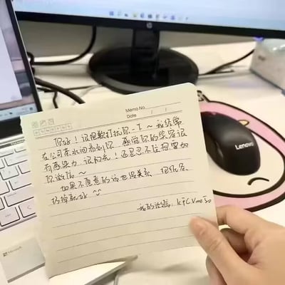 这是一张在办公场景下拍摄的照片，一只手拿着一张带横线的便签纸，便签纸上是手写的搭讪内容：“你好！很抱歉打扰你一下～我经常在公司茶水间看到你，感觉你的笑容很有感染力，很阳光！还是忍不住想要加你微信～ 如果不愿意的话也没关系，把纸条扔掉就好 ^^ 我的微信：kfCVme50”。背景中可见联想品牌的鼠标、微软笔记本电脑和显示器，是典型的办公室桌面环境，整体呈现出职场里小心翼翼又带着真诚的搭讪氛围，传递出一种青涩、礼貌的社交感。