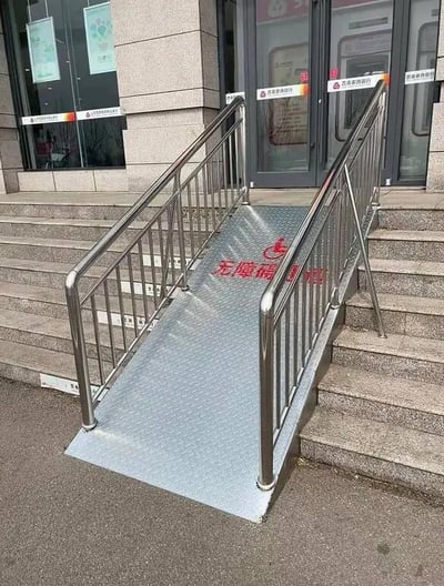 这张图片展示了一个为残障人士设计的无障碍坡道，但坡道尽头直接接到台阶上，完全无法发挥应有的无障碍功能。该设计反映出形式主义，对外显得贴心，实际无用，被网友用来调侃社会工程中的表面文章。双关点在于这种“贴心”服务仅停留在表面，具备强烈逗趣和讽刺效果。