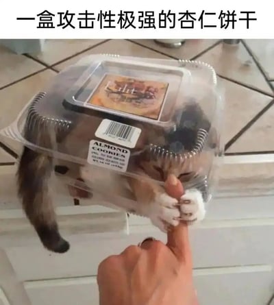 这张实拍图中，一只猫咪钻进了印有“ALMOND COOKIES（杏仁饼干）”字样的透明塑料食品包装盒里，仅露出尾巴和部分头部。画面下方有一只手伸出手指逗弄猫咪，猫咪立刻用两只白色的前爪紧紧抓住这根手指，做出类似“攻击”的动作。图片上方配有中文文案“一盒攻击性极强的杏仁饼干”，将猫咪拟人化调侃成这盒“饼干”，利用猫咪的可爱举动和包装盒的结合制造出反差感，充满趣味和搞笑氛围。