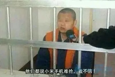 这是一张经过P图改编的静态单图，画面主体是一名穿着橙蓝相间囚服样式服装的男子，被置于类似监狱的铁栏杆之后，面前有一个黑色麦克风，模拟接受采访的场景。图片底部配有白色文字：“他们都说小米手机难抢，我不信！”。该图通过将男子“关押”的场景与小米手机难抢的调侃文字结合，用夸张、戏谑的方式，讽刺早期小米手机发售时抢购难度极大的情况，营造出一种“不信邪去抢手机结果‘锒铛入狱’”的搞笑反差感，属于数码圈的玩梗内容。