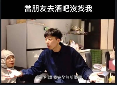 图片上方有文字'當朋友去酒吧沒找我'，下方是厨房场景中，一名穿蓝色外套的男子摊开双手，嘴上说着'我無所謂 我完全無所謂啊'，表情和动作却透露出明显的在意，旁边还有一名戴灰色连帽衫的男子看着他，整体营造出一种口是心非的搞笑氛围。