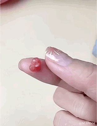 这是一个视觉错位的GIF动图，画面中一根人类手指的指头上放置着一小簇石榴籽，在特定的拍摄角度下，石榴籽的形态和位置看起来像是手指受伤破损的伤口；随着手指的轻微移动，能看清实际是石榴籽，制造出有趣又有点唬人的视觉错觉效果。