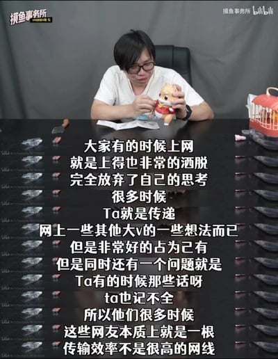 这是bilibili平台up主摸鱼事务所的视频截图，画面中一位戴眼镜的男性主播坐在深色桌前，双手摆弄着一个身着红色服饰的卡通动物玩偶，桌上还摆放着小铲子模型、小物件以及一个红色的小笼子状物品。画面中央叠加了大段白色字幕，以幽默调侃的语气吐槽部分网友上网时完全放弃独立思考，只是照搬甚至记错网络上其他大V的观点，将这类网友比喻成“传输效率不是很高的网线”，点出网络上存在的盲目跟风、缺乏思辨的现象。