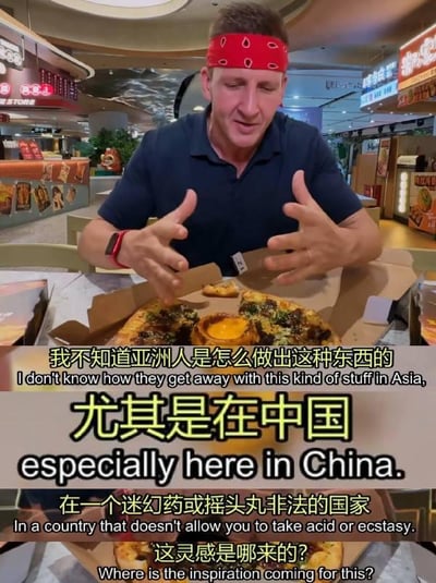 图片中一名戴着红色头巾的外国男子坐在餐桌前，面前放着一个打开的披萨盒，里面有看起来很有特色的披萨。他双手摊开，表情夸张地似乎在对面前的食物表示惊讶或不解。图片上叠加了中文字幕和英文字幕，内容涉及对亚洲尤其是中国美食创意的不当联想和疑问。