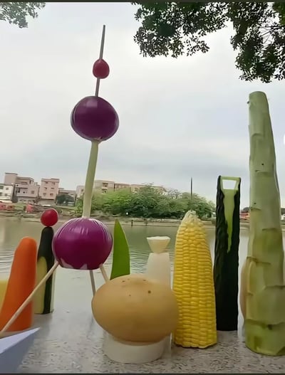 在河边的台面上，创作者用洋葱、玉米、土豆、胡萝卜、黄瓜等常见食材，通过拼接、简单雕刻的方式，搭建出类似城市建筑群、火箭发射塔的创意造型，背景是河流、绿树与居民楼，将普通的日常食材玩出了充满趣味的创意花样，展现了十足的动手能力和想象力，没有双关或谐音梗等隐含内容。