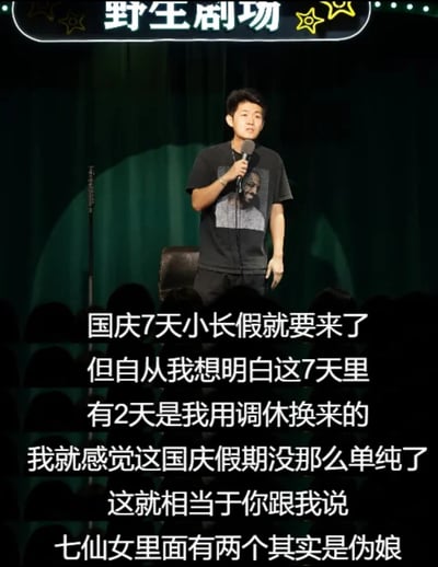 这是一张线下脱口秀演出的现场实拍图，舞台上的脱口秀演员身着印有图案的黑色短袖T恤，手持麦克风站在聚光灯下表演，背景是深色的舞台幕布，台下可见观众的黑色剪影。舞台顶部有带星星装饰的“野生剧场”标识。演员正在表演一段关于国庆假期的脱口秀段子，吐槽国庆7天假期中有2天是通过调休获得的，并用“七仙女里有两个是伪娘”的搞笑比喻，调侃假期的“水分”，用幽默的方式表达出打工人对调休的无奈与吐槽，容易引发职场人群的共鸣。
