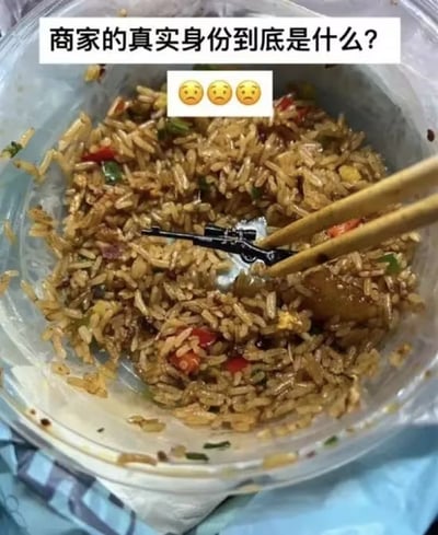 图片展示一碗装在透明塑料碗中的炒饭，米饭粒粒分明，混合有红椒、青椒等配料，一双筷子正夹起饭粒，而饭中竟混入一个黑色玩具枪模型。图片顶部配有文字“商家的真实身份到底是什么？”，下方紧跟三个😰（惊恐）表情符号。该图通过谐音梗“枪杆子里出炒饭”（改编自“枪杆子里出政权”）制造幽默效果，以炒饭中意外出现的“枪”元素夸张调侃商家，引发对“商家真实身份”的戏谑式疑问。