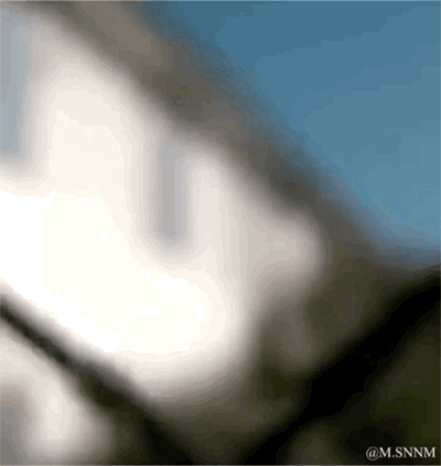 这是一张动态图（GIF），画面起始为极度模糊的色块，随着动图播放逐渐变得清晰，最终显现出动画《进击的巨人》中无垢巨人的面部，背景可见蓝天，整体模拟了近视人群戴上眼镜后看清事物的视觉体验，用动漫IP元素制作趣味效果，没有双关或谐音梗。