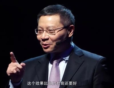 这是一张学者张维为的公开演讲视频截图，画面中他身着深色西装、佩戴眼镜，右手食指向上抬起，正处于演讲的表达状态，似乎在强调自身观点，画面底部配有字幕“这个效果比党的教育还要好”。