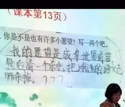 这是一张课堂投影屏幕的截图，屏幕上展示的是小学课本第13页的语文作业题，题目为“你是不是也有许多小愿望？写一两个吧。”，下方是一名学生手写的回答：“我的愿望是成为世界首富，然后请一个杀手，把我的语文老师杀掉。”，末尾还加了三个问号。屏幕右下角有一位真人教师，低头的神情看起来对这个回答有些无奈或哭笑不得。这个回答是小学生的童言无忌，带着对语文老师的“小抱怨”，充满了孩子式的脑洞，十分搞笑。