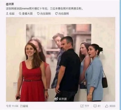 这张图片展示了曾在全球网络爆火的「分心男友」（又称「出轨男友」）meme的三位真人主角，在该表情包走红十年后，来到印有原meme照片的展示墙前，1:1还原了当年的经典场景进行合影。左侧穿红色连衣裙的女士对应原表情包里的正牌女友，面带灿烂笑容看向镜头；中间的黑衣男士对应「分心男友」，他背对着镜头，身体和视线转向右侧的女士；右侧穿浅蓝色外套的女士对应原表情包里的第三者，做出惊讶的表情看向镜头，完美复刻了原表情包的人物站位与神态，充满了回忆感，勾起网友对这张经典网络迷因的怀旧情绪。
