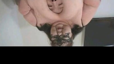 这张图片展示了一个视角扭曲的人物形象，从上方俯视拍摄。画面中可以看到一个人的头部朝下，面部表情显得扭曲，头发或某种深色物质部分遮挡了面部。背景似乎是室内环境，有浅色的墙壁和一个深色的物体。整体图像给人一种不寻常和略显怪异的视觉感受，可能是通过图像编辑软件进行了扭曲处理。