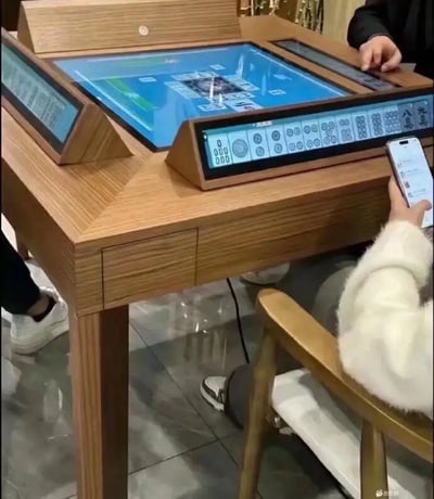 这是一张展示现代电子麻将桌的照片，传统麻将通过多块电子屏幕体现，桌面与每位玩家面前都有独立显示区，彻底改变了手动摸牌的方式。现场三人互动，有人还用手机，体现了现代社交、娱乐和科技的结合。画面给人科技感和创新感，又有一些轻松有趣，显现传统休闲活动的数字化升级。图片未直接包含谐音梗或暗示，不过场景有一种幽默——连打麻将都被“数字浪潮”席卷了。