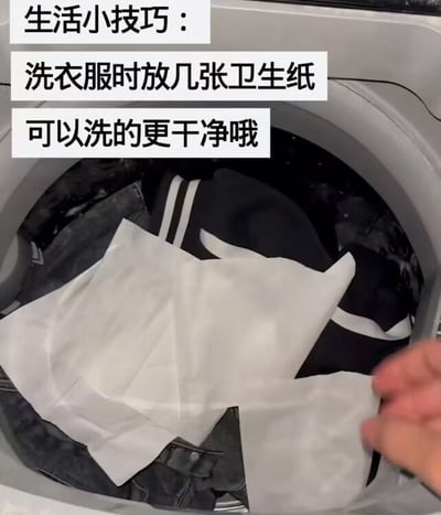 图片展示了一台正在运行的洗衣机，内部有深色衣物，一只手正将白色卫生纸放入洗衣机中。图片上方配有文字“生活小技巧：洗衣服时放几张卫生纸可以洗的更干净哦”，旨在推广这一洗衣技巧。