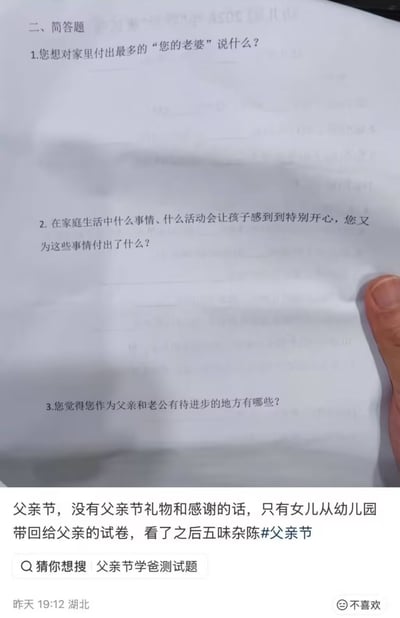 这张图是社交媒体分享内容的截图，画面上半部分是纸质简答题试卷的局部，可见三道针对男性作为丈夫、父亲身份的问题，分别是询问其想对为家庭付出最多的妻子说的话、能让孩子开心的家庭活动及自身的相关付出、作为父亲和丈夫有待进步的方向，试卷右下角露出按压试卷的人的手指；画面下半部分是发布者配文，内容为父亲节当天该发布者（父亲）没有收到礼物和感谢话语，只收到了女儿从幼儿园带回的这份试卷，看完后心情五味杂陈，附带#父亲节话题，下方还有“猜你想搜：父亲节学爸测试题”的平台提示，以及发布定位湖北、发布时间为昨日19:12的信息。