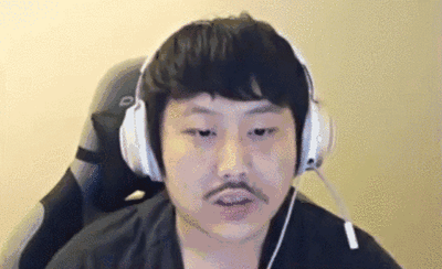 这是一段从网络直播画面中截取的动态GIF，图中男性主播戴着白色头戴式耳机，坐在电竞椅上，面部表情呆滞，嘴巴微微动着，看起来带着疑惑与无奈的情绪，仿佛在直播过程中遇到了让他摸不着头脑的状况，画面真实接地气。