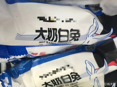 图片展示了几袋蓝白配色的冰淇淋包装袋，正面印有黑色大字“大奶白兔”及英文“MILK RABBIT ICE CREAM”，旁边配有与经典“大白兔奶糖”相似的兔子图案。部分品牌信息被像素化处理。该包装明显模仿知名品牌“大白兔”的设计风格，但名称改为具有调侃意味的“大奶白兔”，属于山寨或恶搞产品，常被用于社交媒体吐槽假冒伪劣商品的迷惑行为。