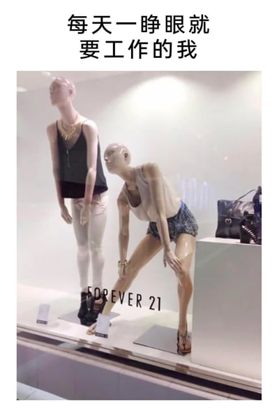 这是一张经过文字改编的实拍梗图，原始场景是快时尚品牌FOREVER 21的线下门店橱窗，橱窗内的两个人体模特呈现出疲惫无力的姿态：一个身体微微前倾站立，另一个双腿分开弯腰、双手撑在膝盖上。图片顶部添加了文字“每天一睁眼就要工作的我”，用模特的疲惫姿态精准对应打工人刚醒来就要投入工作的身心俱疲状态，以此调侃职场人日常工作的倦怠感，引发职场群体的共鸣。