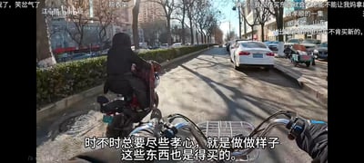 这是B站UP主拍摄的第一视角骑行电动车的冬季城市街景截图，画面中前方有一位身着黑色连帽外套的人骑着旧电动车，道路两侧停满汽车，树木光秃，尽显冬日城市氛围。画面底部配有讽刺性字幕：“时不时总要尽些孝心，就是做做样子，这些东西也是得买的。”，同时画面上还有观众的弹幕评论，如“最孝顺的一集”“出行必备的电动车不肯买新的”等，结合字幕与弹幕，调侃了那种表面标榜尽孝，实则不舍得为家人购置实用新物品的“假孝顺”行为，充满讽刺与搞笑的氛围。