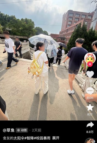 这是一张竖版的短视频平台内容截图，拍摄于晴天的校园户外：多名学生在通往低处的步道上行走，地面有阳光直射形成的清晰人影，其中一名学生撑着通常用于雨天的透明雨伞，背景可见红砖教学楼、高大乔木、白色栏杆等校园景观。画面右侧是平台互动功能区，显示获赞7.3万、评论4505条、收藏822次、转发8.9万次；页面底部标注发布者为用户“草鱼”，发布于2天前，配文将雨天用的透明伞调侃为太阳伞，还带上了“校园暴雨”的话题，以配文和实际晴天场景的反差制造笑点，调侃舍友误把雨伞当遮阳伞使用的迷糊行为。