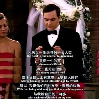 这是一张美剧《生活大爆炸》的视频截图，画面呈现的是婚礼场景：穿着黑色礼服的谢尔顿·库珀双手拿着物品，低头专注地看着，似乎在念致辞内容；左侧是身着红色抹胸礼服的佩妮，神情平静地站在一旁，目光看向下方。图中配有中英双语字幕，中文内容是谢尔顿对于亲密关系的独特发言：他表示无法理解“人穷尽一生寻找另一个人共度一生”的行为，认为自己本身足够有趣无需他人陪伴，最后真诚祝福新人能在对方身上获得和自己独处时一样多的快乐。这段发言既贴合谢尔顿古怪直白的人物设定，又传递出温暖的心意，是剧中的经典名场面。
