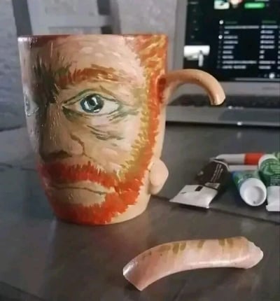 图片中展示了一个创意手工马克杯，杯身被精心绘制为文森特·梵高的肖像，还原了他标志性的红色胡须、深邃的蓝色眼睛和严肃的面部表情。马克杯的把手已断裂，断裂的把手部件孤零零地躺在桌面上。杯子周围散落着几支不同颜色的颜料管，背景中可见一台打开的笔记本电脑，屏幕显示着模糊的界面。整体场景呈现出一种艺术创作过程中意外损坏作品的惋惜感，兼具创意与生活化气息。