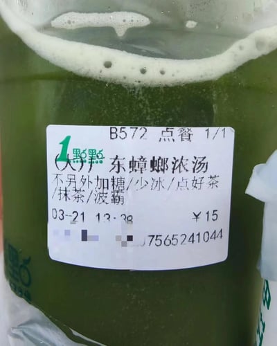 这是一杯一点点品牌的抹茶波霸奶茶，杯身的订单标签被网友恶搞修改，将原本的饮品名称替换为「(大)广东蟑螂浓汤」，保留了「不另外加糖/少冰/点好茶/抹茶/波霸」的饮品规格，同时标签上还显示订单号B572、价格15元、制作时间03-21 13:38等真实订单信息。<br>这是利用广东地区关于蟑螂的网络地域梗制造的恶搞内容，用正常奶茶和离谱名称形成强烈反差，达到搞笑效果。