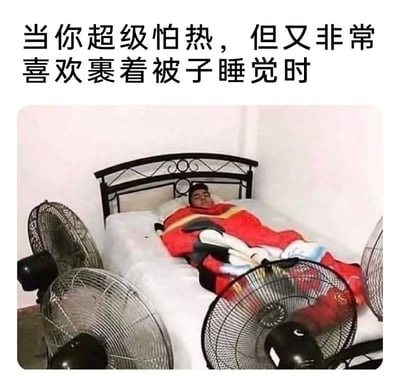 图片上方配有文字'当你超级怕热，但又非常喜欢裹着被子睡觉时'，下方是一张实拍照片：床上躺着一个人，全身裹在红色被子里，而床的周围摆放着多台电风扇，正对着人吹风。画面幽默地展现了怕热却又离不开被子的矛盾睡眠状态。