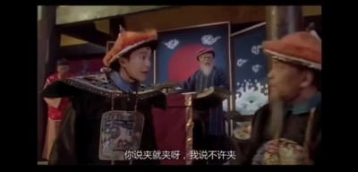 这是一张香港喜剧电影《九品芝麻官之白面包青天》的视频截图，采用剧场式构图展现公堂对峙场景。画面中，身着清代官服的包龙星（周星驰饰演）表情激动，身体前倾，正大声反驳对面的官员，台词“你说夹就夹呀，我说不许夹”体现出他在公堂上试图主导审案节奏、对抗阻挠者的状态；右侧的对立官员表情严肃，看向包龙星，形成对峙之势；背景里还有站在公堂案台后的老者以及角落的人物，还原了古代公堂的审案场景，整体氛围充满了无厘头的对抗感，是电影中极具冲突感的名场面之一。