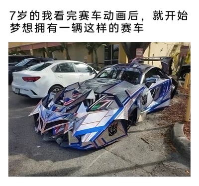 这是一张带有反差搞笑效果的图文混排梗图，上方配文“7岁的我看完赛车动画后，就开始梦想拥有一辆这样的赛车”，下方是一辆停在停车场的汽车：它原本是严重损毁的事故车，被人用类似变形金刚狂派（霸天虎）风格的装饰改装，外观造型破碎尖锐，采用蓝银配色还带有狂派标志，看起来完全是动画里酷炫赛车的“现实荒诞版”。整图通过童年美好梦想与现实中怪异改装车的巨大反差，制造出强烈的搞笑效果，调侃童年梦想在现实里的离谱落地。