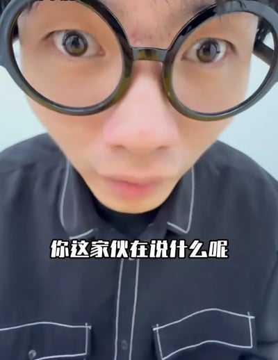 图片为近距离拍摄的真人面部特写，人物佩戴黑色圆形大框眼镜，穿着带有白色缝线装饰的黑色衬衫。人物双眼睁大，眉毛微蹙，表情看起来困惑又带着一丝惊讶，直视镜头。图片底部有白色文字“你这家伙在说什么呢”，表达出对对方言论的不解。