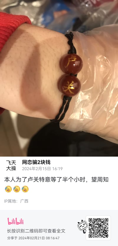 这是B站用户「飞天大操」发布的一条生活分享动态，配图展示了手腕上佩戴的定制款黑绳红玛瑙手链，两颗红玛瑙珠子上分别刻有金色的「卢」「关」二字。用户配文称「本人为了卢关特意等了半个小时，望周知」，并附上三个笑哭表情，以玩笑的语气分享自己为拿到定制手链的经历。